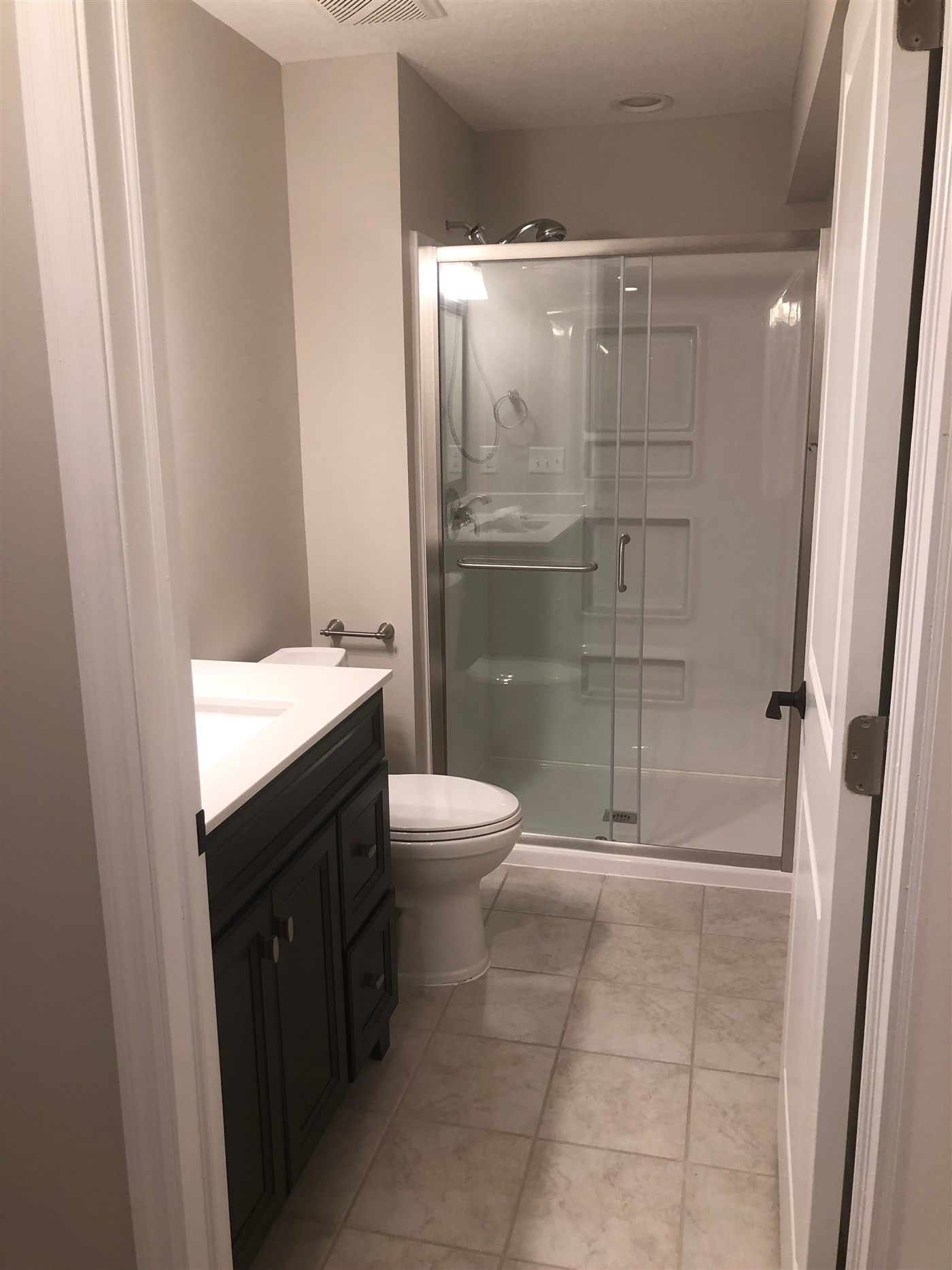 Walk-in shower with sliding glass doors, grab bar and dark vanity in a remodeled Central Ohio bathroom