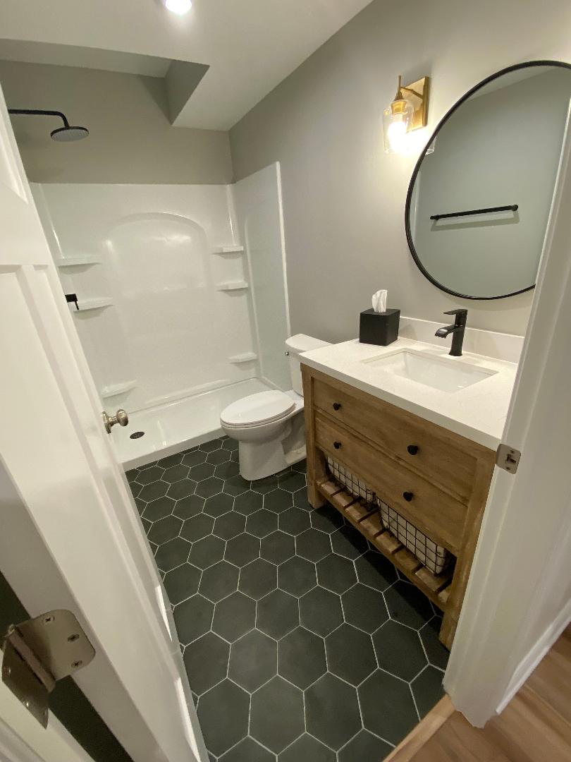 Bathroom with dark hexagon tile floor, wood vanity with quartz top and white shower surround