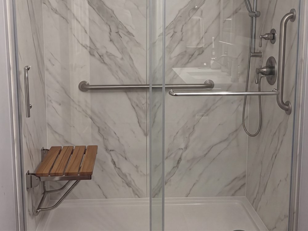 A walk-in shower with Trinity stone-look walls, a sliding glass door, a fold-down seat and grab bars